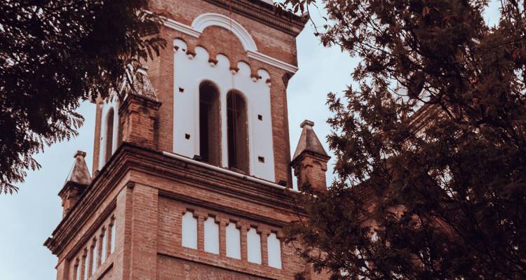 Gros plan d'un clocher d'église historique en brique encadré par des branches d'arbres