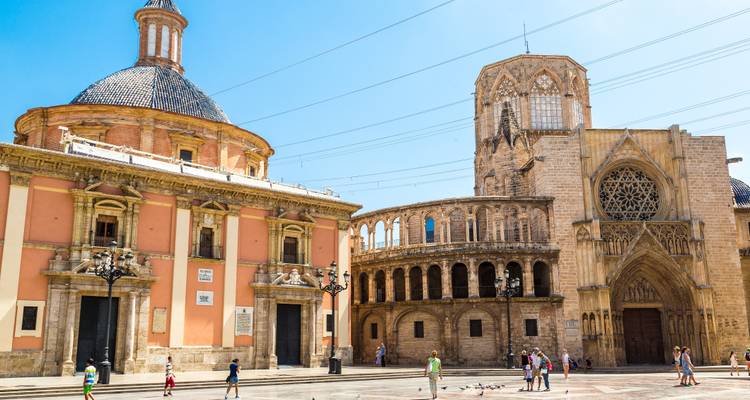 Kathedrale und Basilika von Valencia mit Blick auf einen sonnigen Platz, wo sich Menschen und Tauben versammeln.