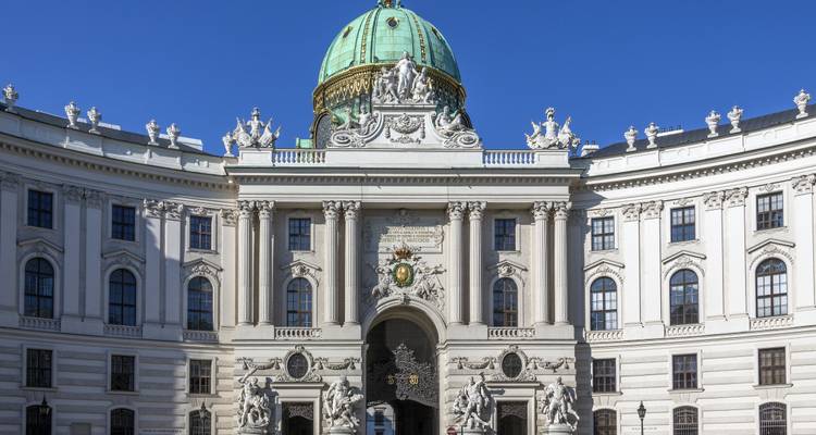 Entrée baroque du palais de la Hofburg de Vienne couronnée par un dôme turquoise sous un ciel bleu clair.