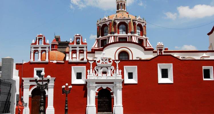 Façade d'église baroque rouge et blanche sous un ciel bleu éclatant à Cholula.
