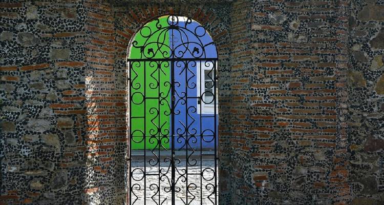 Portail en fer forgé décoratif encadrant un mur vert vif et bleu à l'intérieur d'une arche en brique.