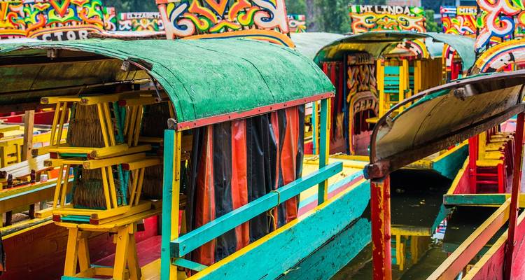 Bateaux à fond plat peints de couleurs vives avec des toits arqués amarrés le long d'un canal calme.
