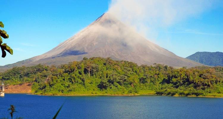 Arenal Volcano emitting a plume of steam above a blue lake and verdant rainforest.
