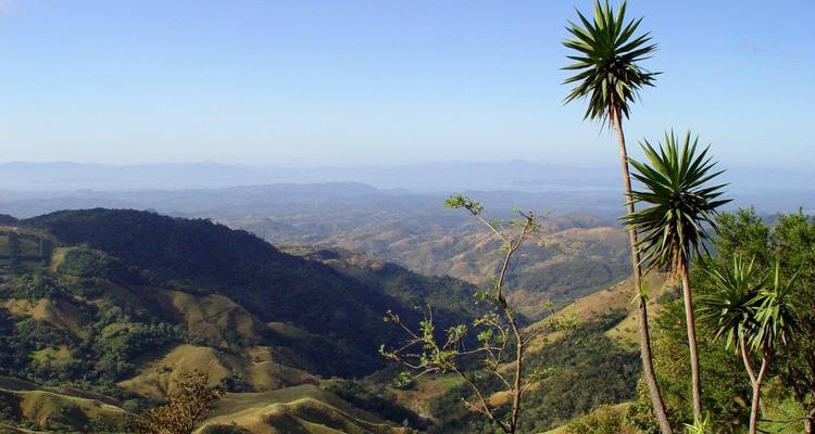 Wide view over rolling green hills and distant mountains under a clear blue sky.