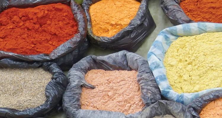 Sacos amontonados de especias molidas coloridas dispuestos en un puesto de mercado.