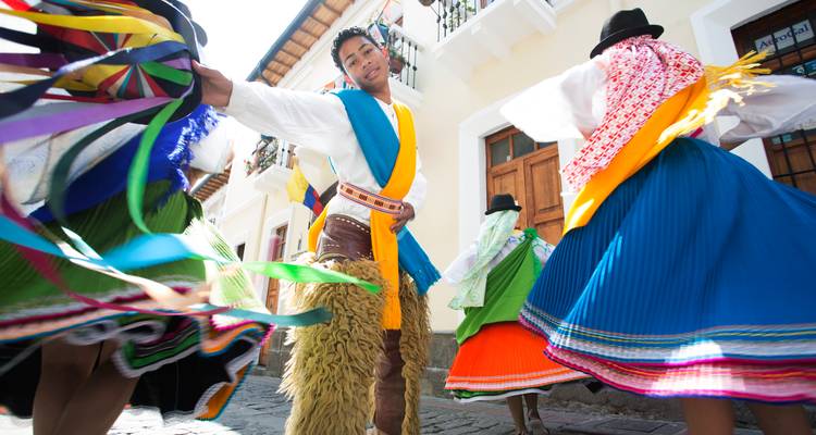 Bailarines tradicionales ecuatorianos coloridos girando con faldas brillantes por una calle empedrada.