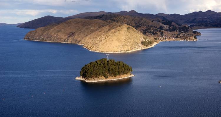 Petit îlot boisé et plus grande péninsule vallonnée émergent des eaux bleu profond d'un vaste lac de haute altitude.