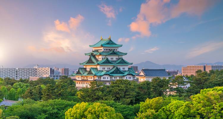 Elegante Nagoya Castle met groene daken die oprijst boven weelderig parklandschap onder een kleurrijke zonsonderganghemel.