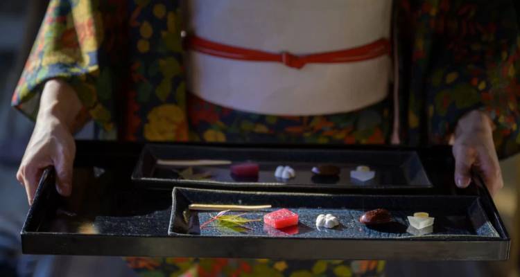 Personne en kimono présentant des plateaux en laque contenant des confiseries japonaises traditionnelles.