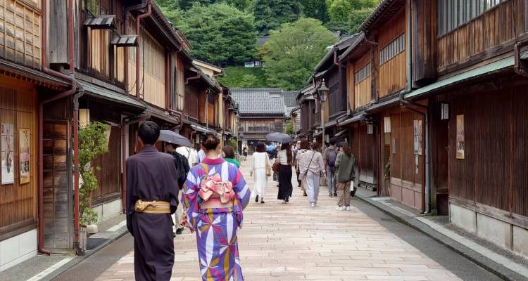Des visiteurs vêtus de costumes traditionnels et modernes flânent dans une rue historique en bois du quartier des geishas.