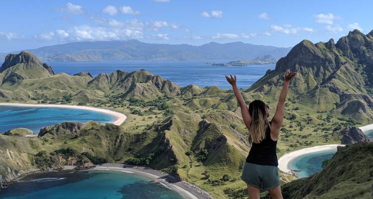 Une femme lève les bras en signe de triomphe au point de vue de l'île Padar surplombant des baies turquoise incurvées.