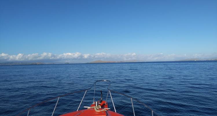 La proue d'un bateau rouge pointe vers l'archipel lointain de Komodo sous un ciel bleu clair.
