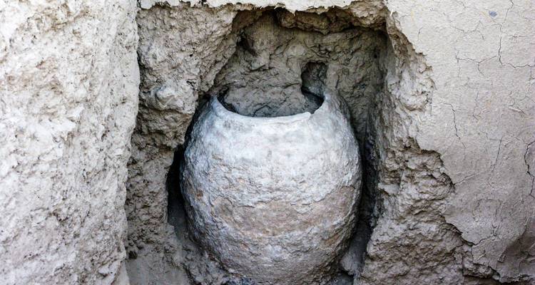 Jarre en céramique ancienne partiellement exposée dans des murs de briques de terre qui s'effritent sur un site de fouilles archéologiques.