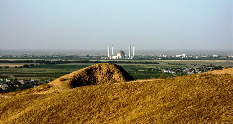 Mosquée au dôme doré vue à travers une vaste plaine depuis des collines sablonneuses.