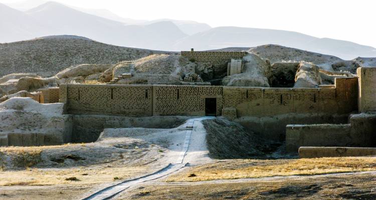 Murs d'adobe fortifiés et porte d'un ancien établissement au milieu de collines arides.