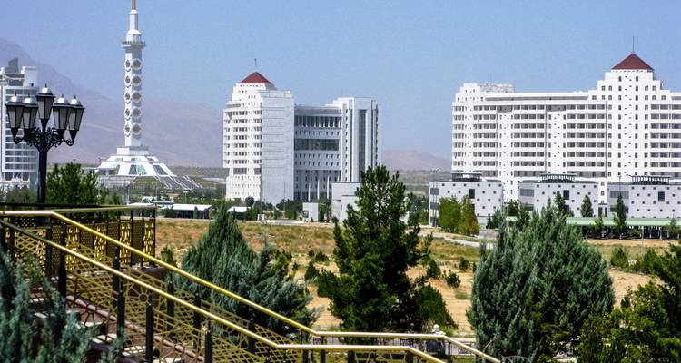 Bâtiments modernes en marbre blanc et une haute tour s'élevant au-delà des jardins urbains paysagers d'Achgabat.
