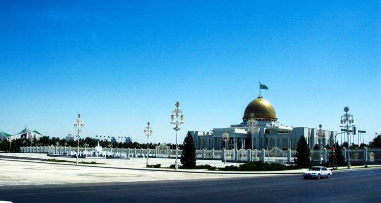 Grand complexe présidentiel avec dôme doré et clôture ornementée le long d'un large boulevard.