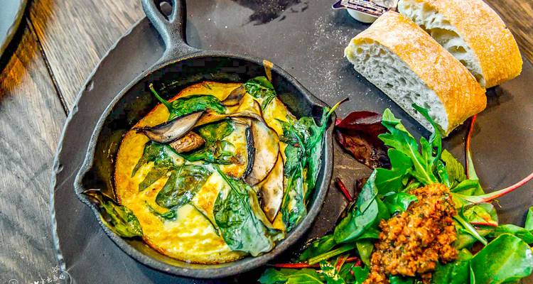 Une poêle en fonte de frittata aux épinards et champignons est servie avec du pain frais et une salade.