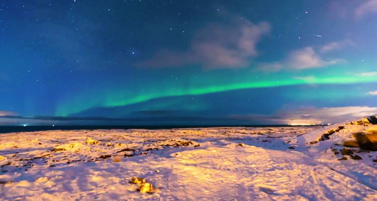 Une aurore boréale d'un vert éclatant balaye un paysage hivernal islandais étoilé.