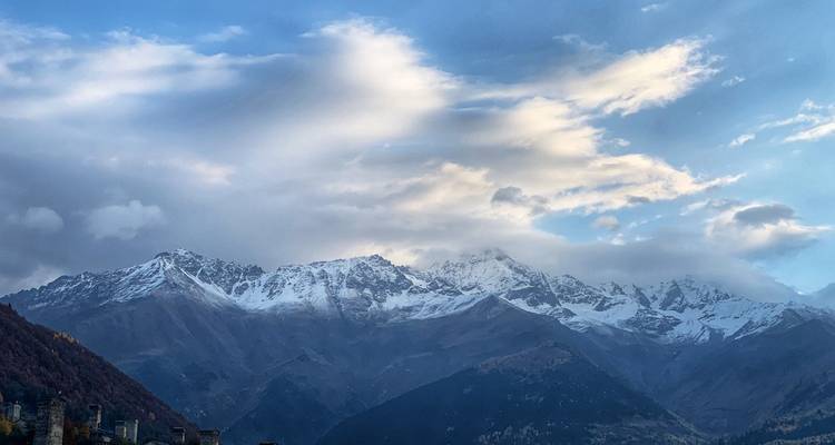 Snow-capped Caucasus mountain range beneath dramatic clouds and late-day light.