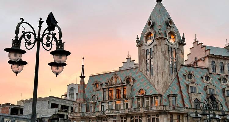 Fairy-tale style building with patterned roof tiles and clock faces glowing at sunset in Batumi.