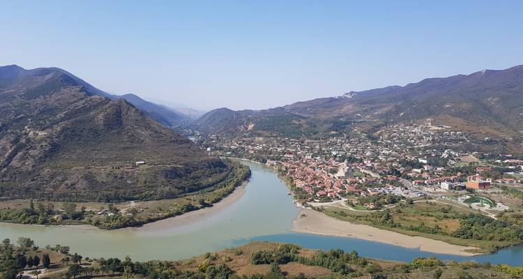 Aerial view of two rivers converging beside a Georgian town nestled among rolling mountains.