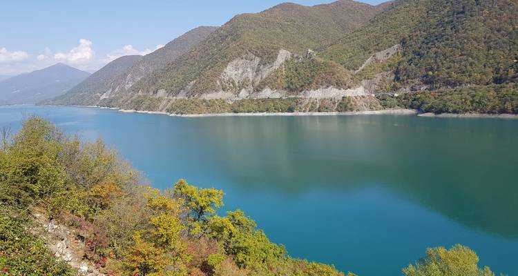 Turquoise reservoir bordered by forested mountains under a clear sky.