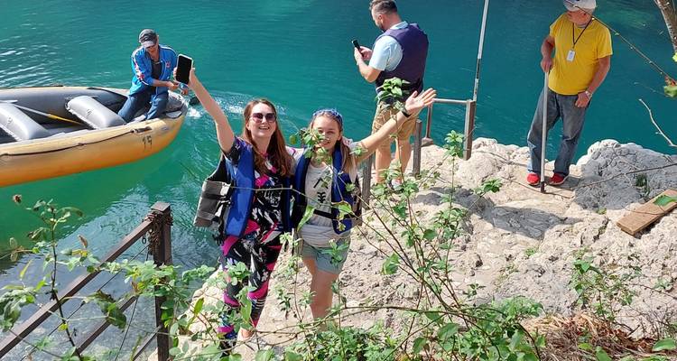 Excited travelers wearing life vests raise their arms beside a small inflatable boat on bright turquoise water.
