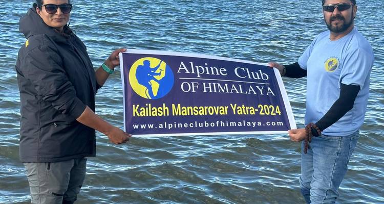 Two travellers waist-deep in lake water displaying an Alpine Club of Himalaya banner