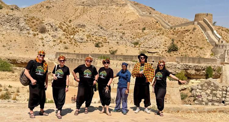 Groupe de touristes en tenues coordonnées pose avec enthousiasme devant les murs en pierre du désert d'un fort perché sur une colline au Pakistan.