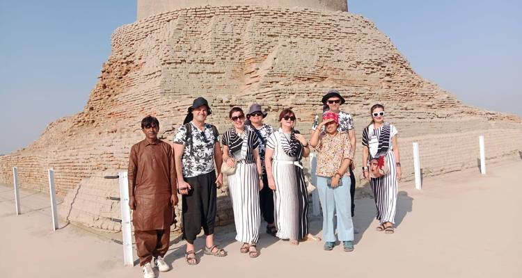 Un groupe de voyageurs se tient devant les ruines massives en brique d'un stupa d'un site archéologique ancien sous un ciel brumeux.