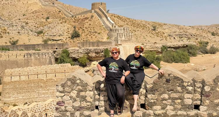 Deux femmes se tiennent sur les remparts d'un fort du désert avec des murs étagés s'étendant sur les collines arides derrière.