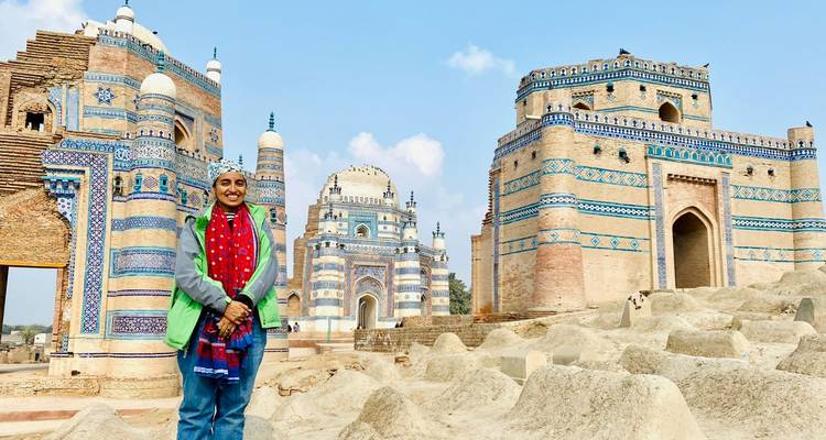 Un voyageur se tient devant un sanctuaire soufi aux carreaux bleus et blancs complexes sous un ciel lumineux.