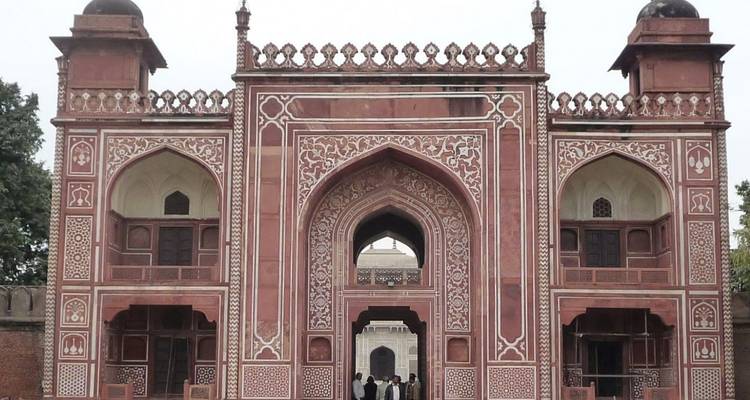 Red sandstone Mughal gateway richly carved with visitors standing below