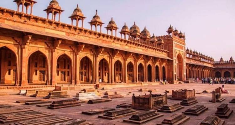 Long colonnaded courtyard in Fatehpur Sikri with rows of old tombstones and afternoon light