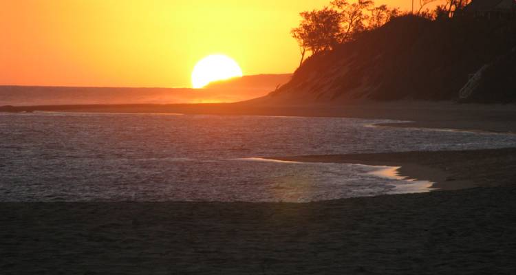 Sol naranja brillante se pone sobre la tranquila costa tropical y acantilado bajo