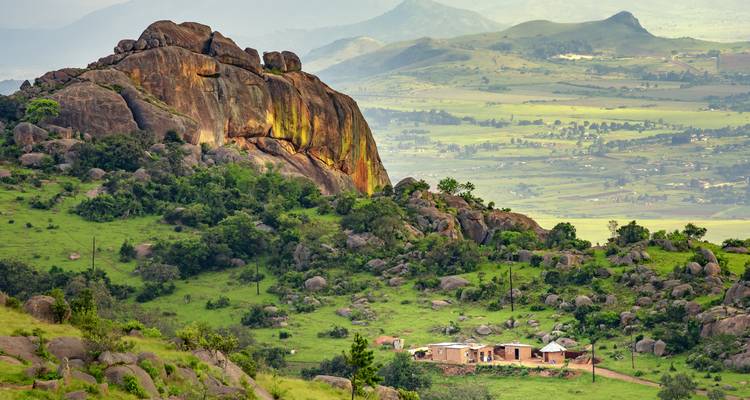 Valle verde salpicado de rocas y casas rurales bajo un monolito de granito en Esuatini