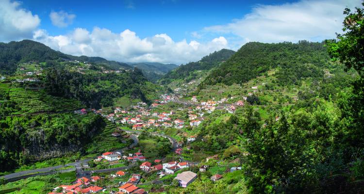 Panoramisches grünes Tal mit rotgedeckten Dörfern und terrassierten Feldern unter blauem Madeira-Himmel