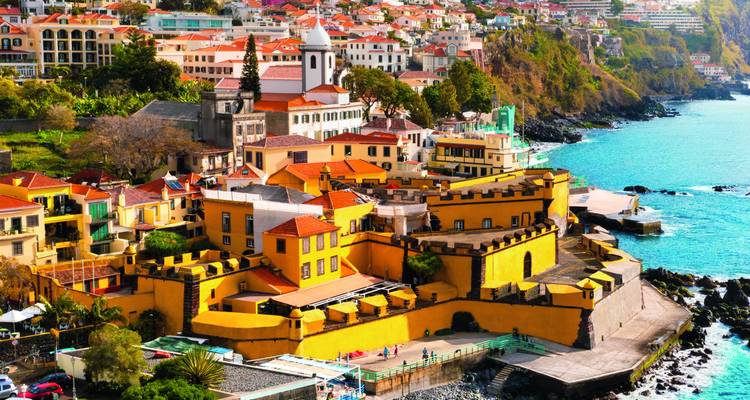 Vue lumineuse sur la vieille ville colorée de Funchal avec la Fortaleza de São Tiago jaune au bord des eaux turquoise de l'Atlantique et des falaises luxuriantes.