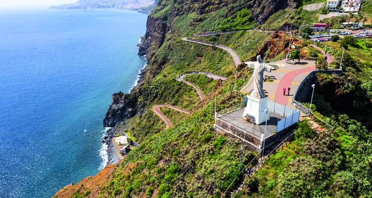 Vue aérienne du point de vue du Cristo Rei et de la route côtière sinueuse au sommet d'une falaise verte spectaculaire au-dessus des eaux bleu profond de l'Atlantique à Madère.