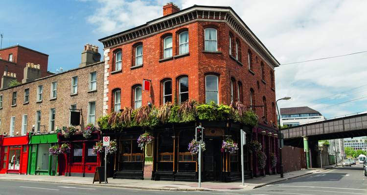 Traditionelle rote Backsteineckenkneipe geschmückt mit hängenden Blumenkörben an einer sonnigen Dubliner Straße