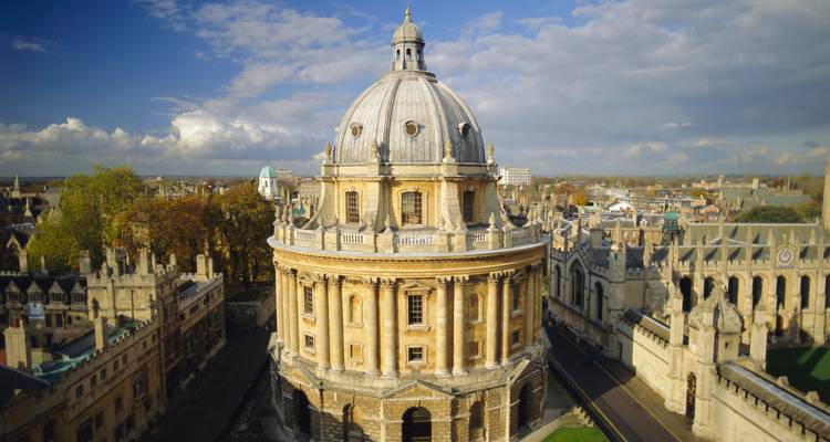 Luftaufnahme der kreisförmigen Radcliffe Camera in Oxford, umgeben von historischen Colleges unter einem teilweise bewölkten Himmel.