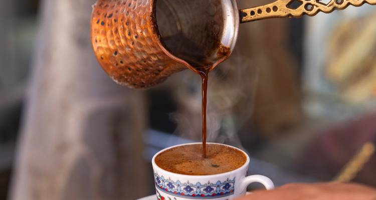 Traditionelle Kupfer-Cezve gießt dampfenden türkischen Kaffee in eine Porzellantasse