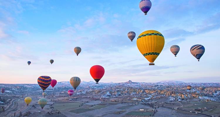 Dutzende farbenfroher Heißluftballons schweben bei Tagesanbruch über Kappadokiens mosaikartige Täler.