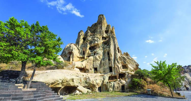 Hoch aufragende erodierte Felsformation mit in den Stein gehauenen Höhlenwohnungen in Kappadokien unter einem strahlend blauen Sommerhimmel.