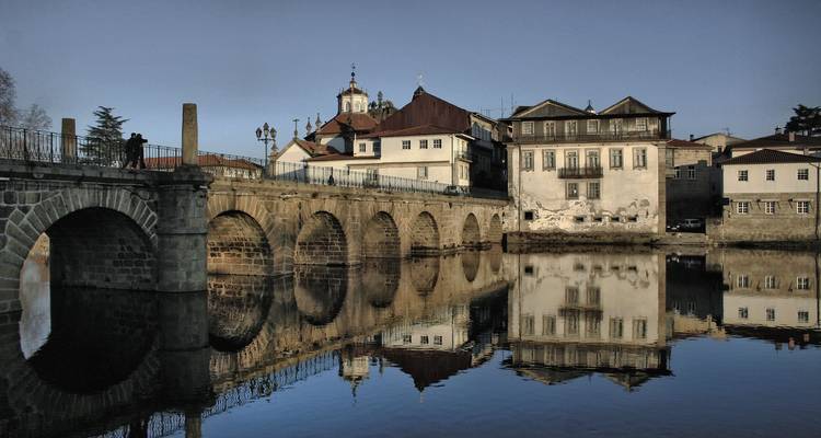 Historische Steinbrücke mit mehreren Bögen, die sich bei Morgendämmerung perfekt im ruhigen Flusswasser spiegelt.
