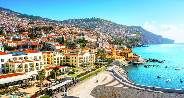 Farbenfrohe Stadtlandschaft von Funchal, die sich über Hügel hinab zu einer strahlend blauen Atlantikküste erstreckt