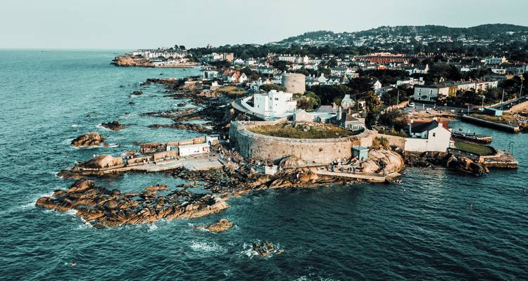 Luftaufnahme einer steinernen Küstenfestung und der umliegenden Küstenstadt auf einer felsigen Halbinsel in Irland.