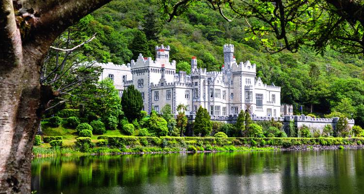 Das märchenhafte Schloss der Kylemore Abbey spiegelt sich in einem ruhigen See wider, umrahmt von üppigen Bäumen und Bergen.