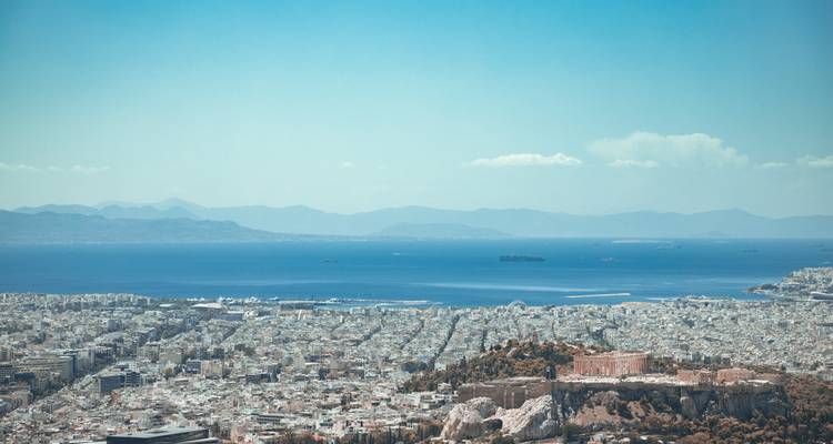 Vue élevée sur Athènes avec les ruines de l'Acropole et la mer Égée s'étendant jusqu'aux montagnes lointaines.